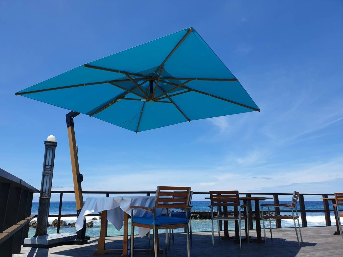 Side-by-side diagram showing traditional center-pole umbrella vs. cantilever rectangular outdoor umbrella highlighting pole obstruction, coverage area, and wind vulnerability