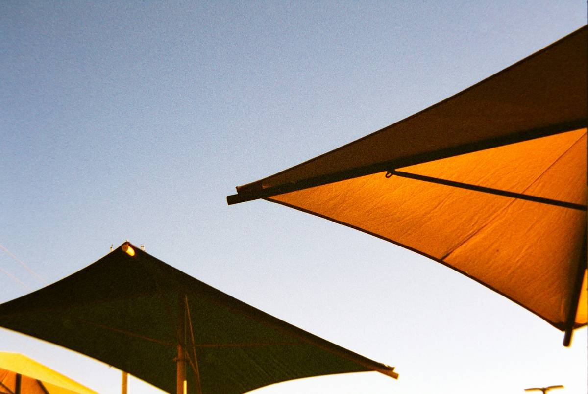 Diagram comparing circular vs. rectangular cantilever umbrella shade coverage over a 10x12 ft patio. Rectangular model fully covers seating area; circular leaves two corners exposed.