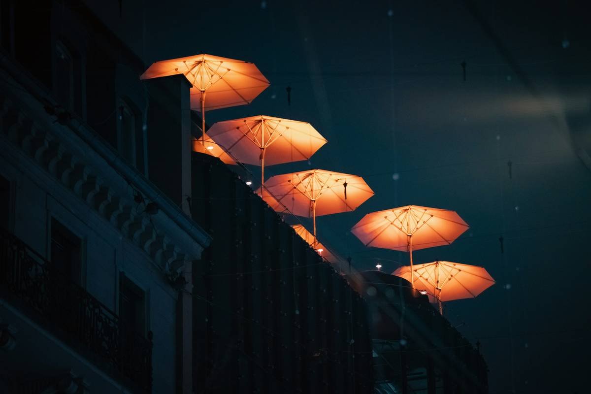 Modern cantilever outdoor umbrella with lights illuminating a patio dining set at dusk
